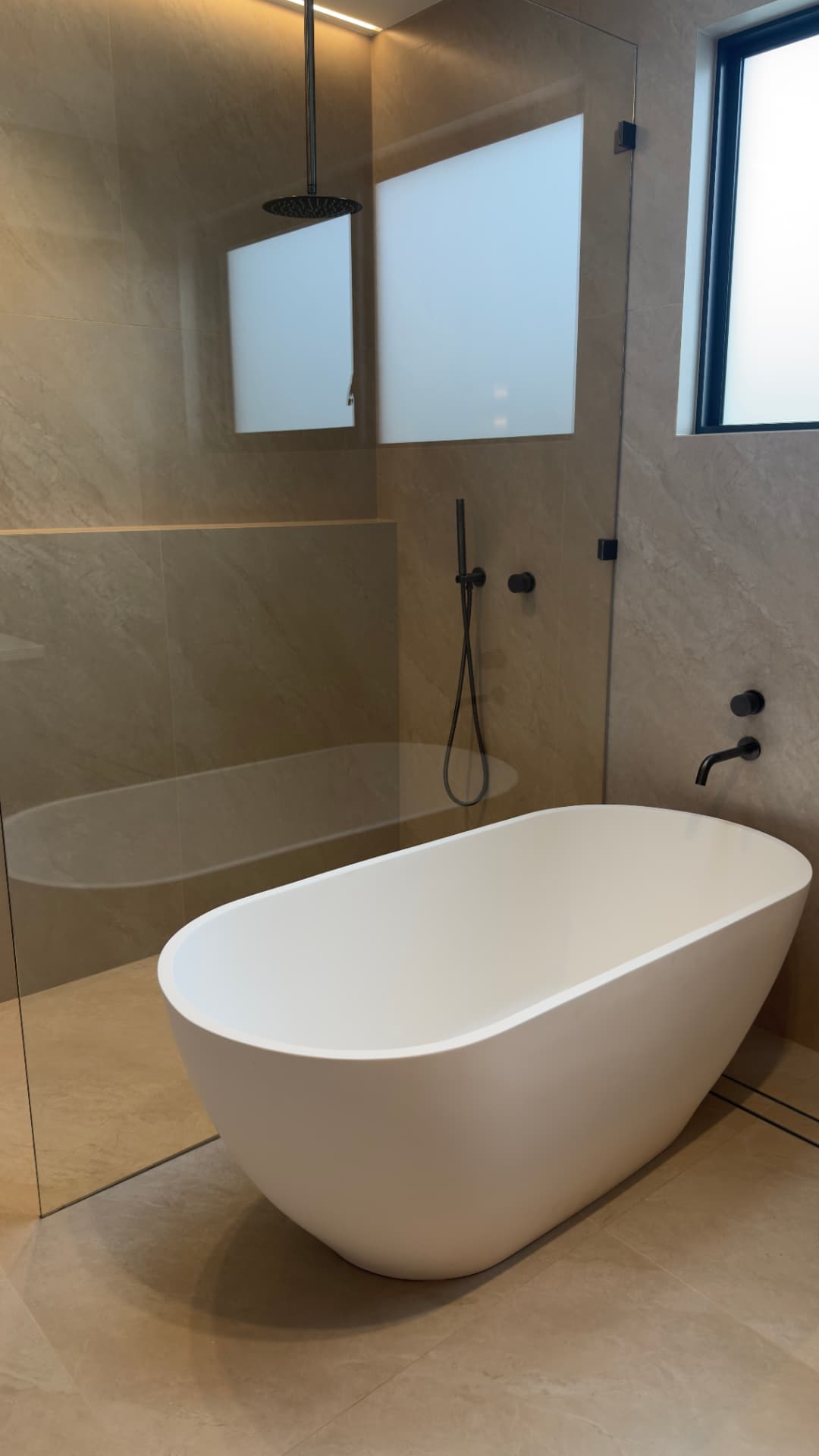 Bathroom with a freestanding bath, clean tiled surfaces and glass shower screen