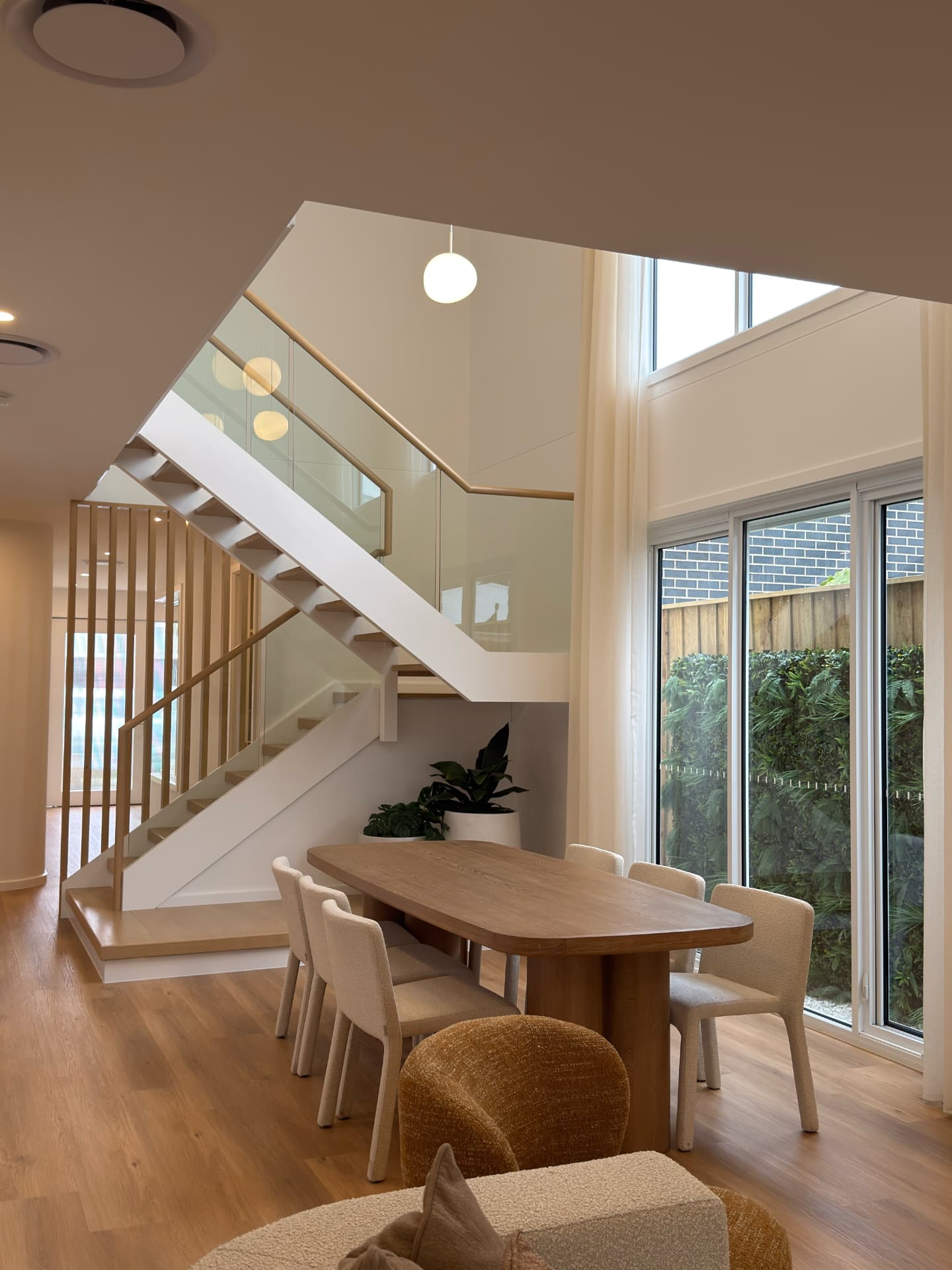 Living and dining area with timber floors, glass balustrades and full-height windows